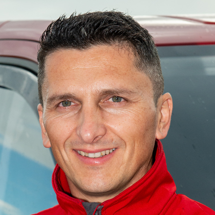 Person in a red jacket standing in front of a vehicle.